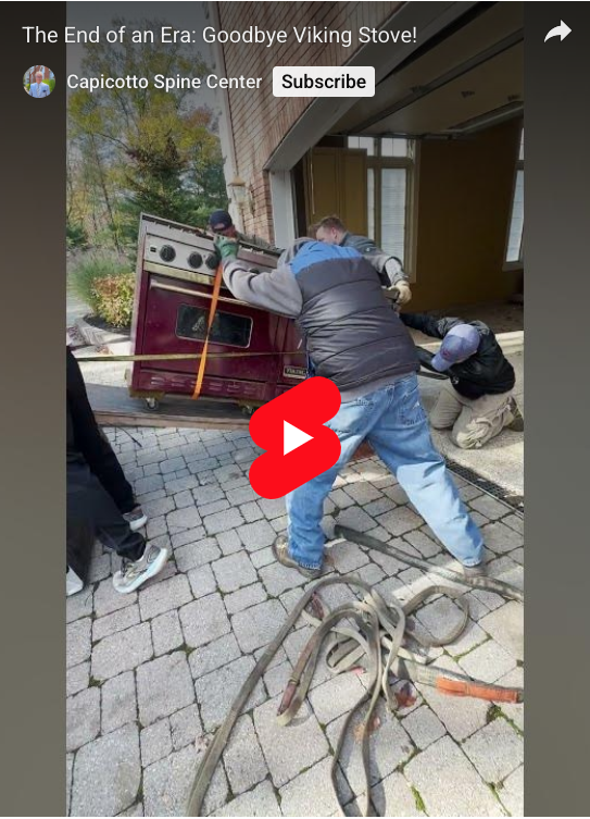 Four men moving a red Viking oven.